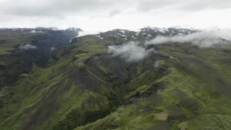 a breathtaking aerial view of a lush green valley surrounded by rugged cliffs and glaciers in hafursey, iceland, under cloudy skies.