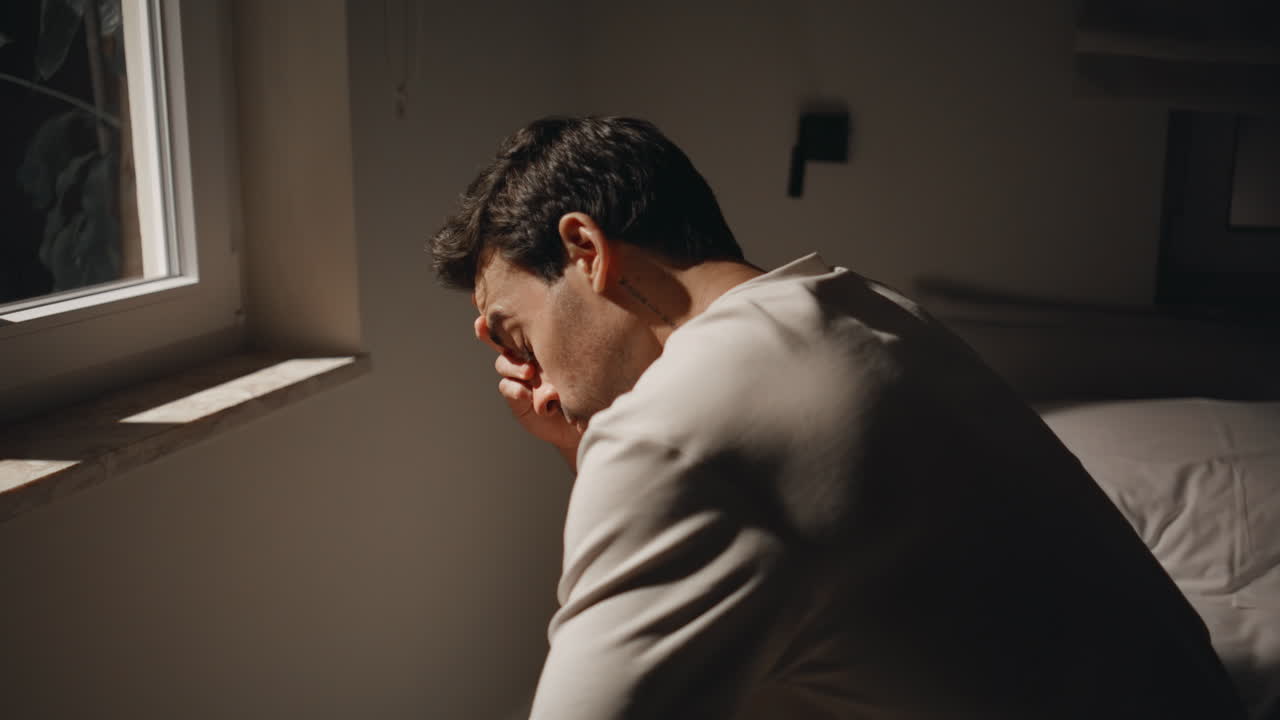 Primer plano de un hombre mirando por la ventana de noche en una habitación con sensación de depresión. Hombre preocupado en la cama