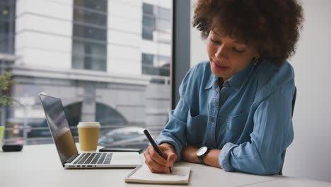 businesswoman in modern office working on laptop and making notes in notebook