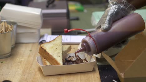 Tomato-and-barbecue-flavored-sauce-squeezed-out-of-bottle-onto-freshly-grilled-meat,-filmed-in-slow-motion-as-close-up-shot