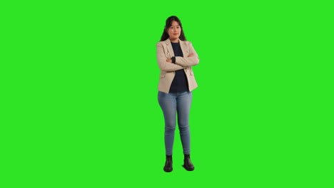 full length studio portrait of female teacher or businesswoman standing against green screen folding arms