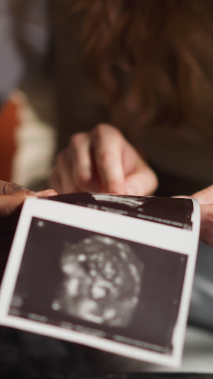 Young couple of white woman and African-American man partner holds ultrasound pictures of expecting baby in living room extreme closeup slow motion