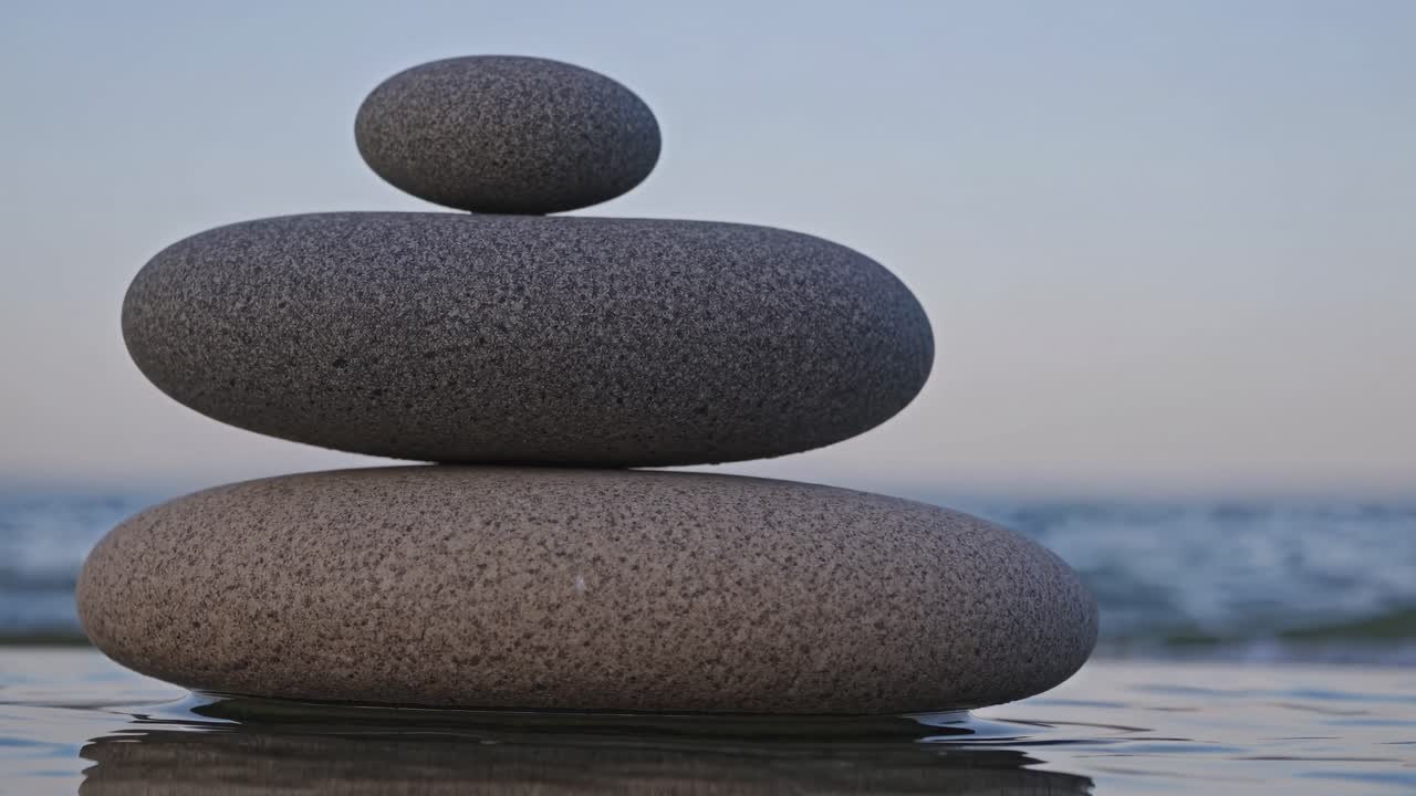 Close-up video of smooth stones stacked in balance, shot from a low angle, against a serene ocean