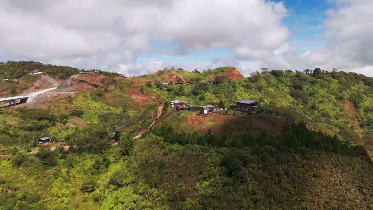 Drone view of modern vacation homes perched on a green mountain ridge. Scenic highland landscape featuring rural development and infrastructure construction in Marilog District, Davao