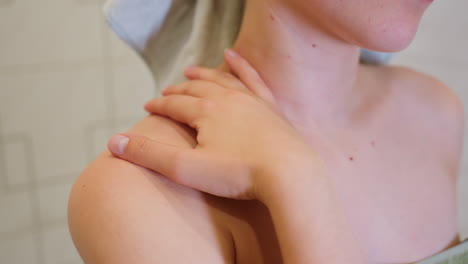 Close-up view of woman massaging her neck in bathroom, performing a soothing self-care routine, she appears relaxed, focusing on gentle massage for skin health and stress relief