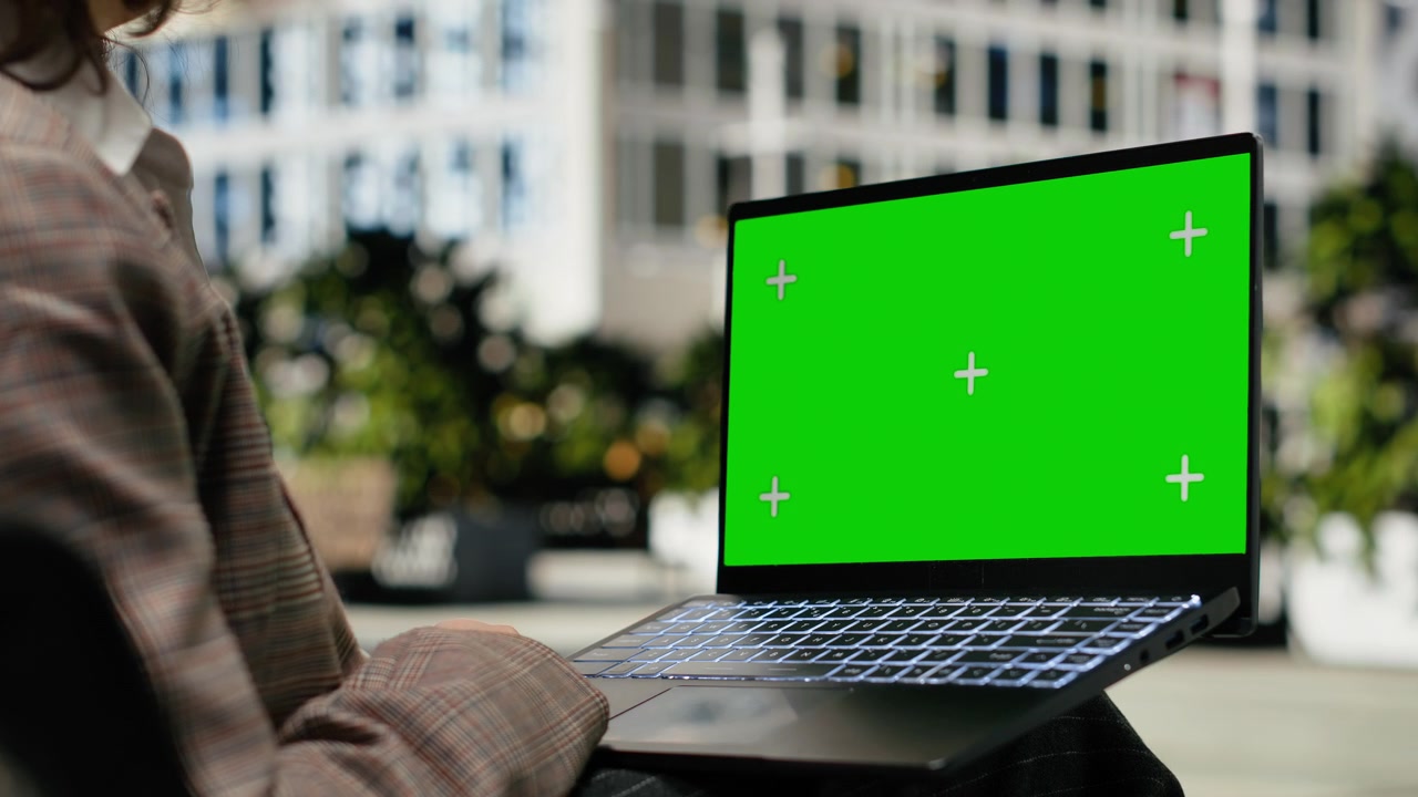 Laptop con schermo verde utilizzato da un lavoratore su una panchina di legno del parco all'aperto