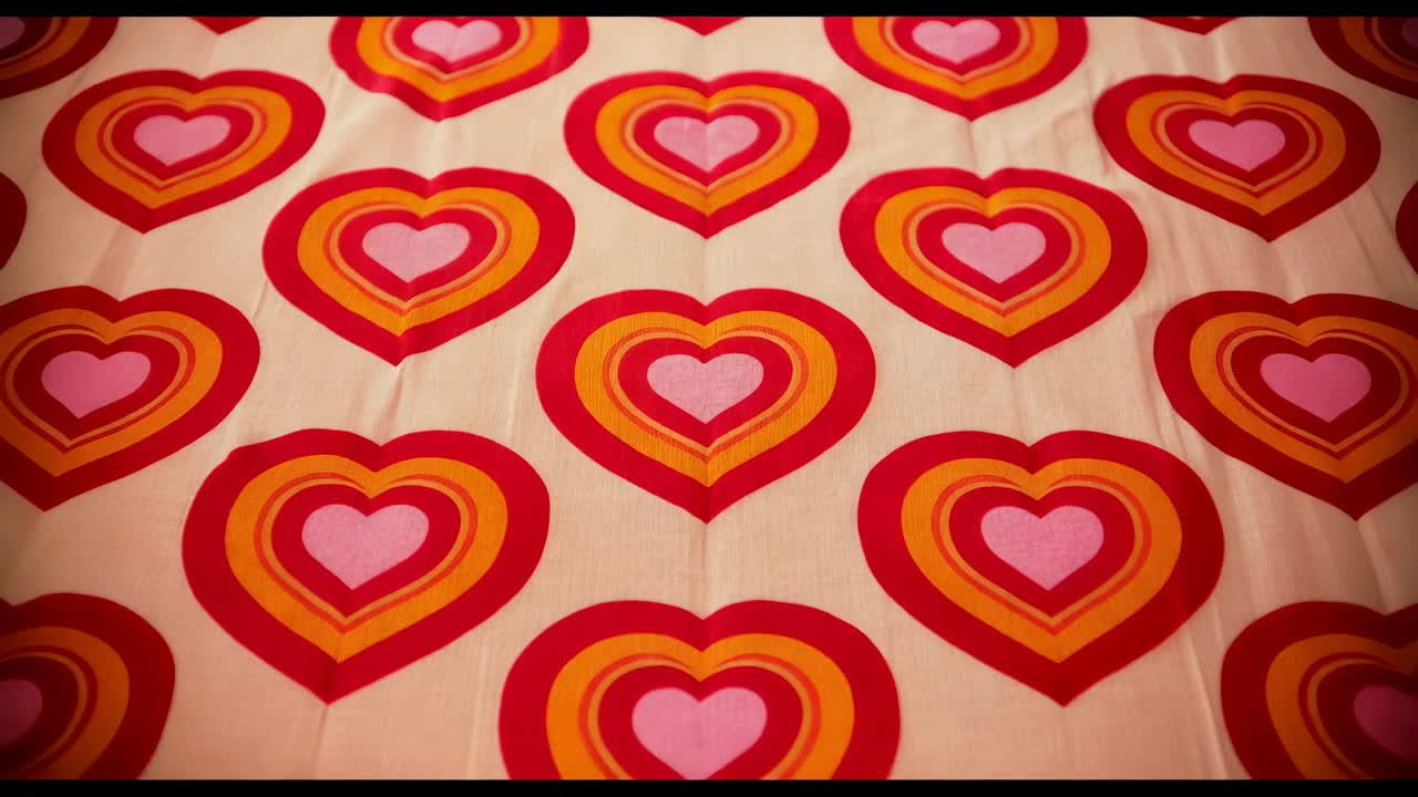 Starting camera move, focusing closer on heart bedspread with bars, revealing central crease