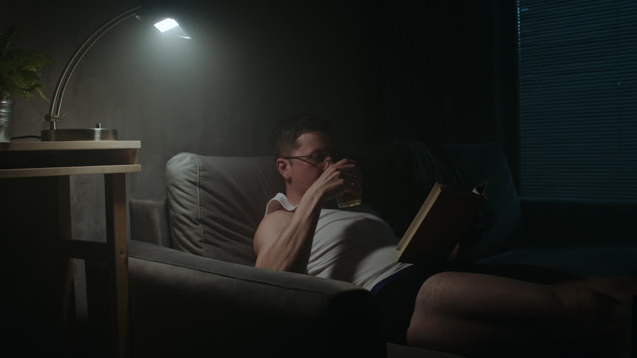 A sad man reads a book at night in his underwear