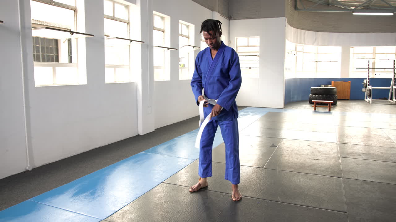 Practicing judo, man in blue gi adjusting belt in dojo