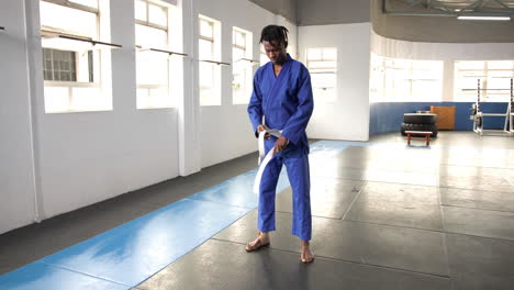 practicing judo, man in blue gi adjusting belt in dojo