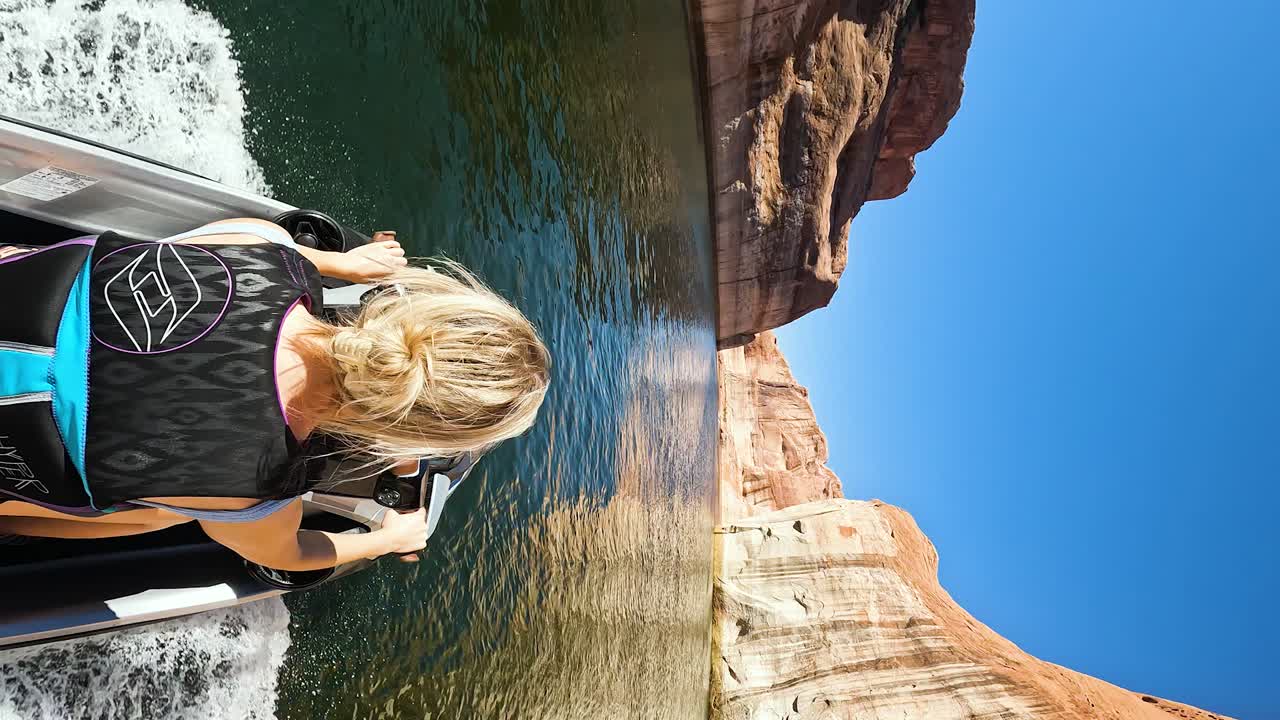 mujer de cabello rubio conduciendo jet ski en el cañón del lago powell, tiro vertical pov