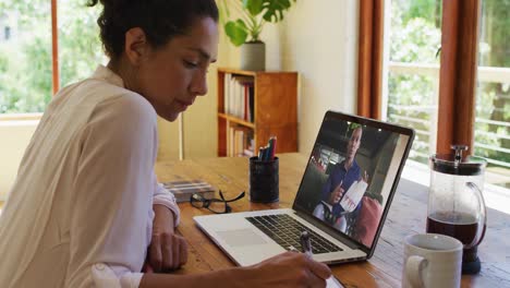 african american woman taking notes while having video call with male colleague on laptop at home