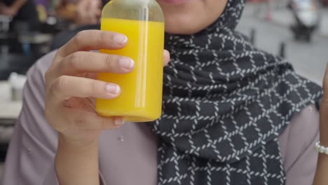 woman in hijab drinking orange juice at a cafe