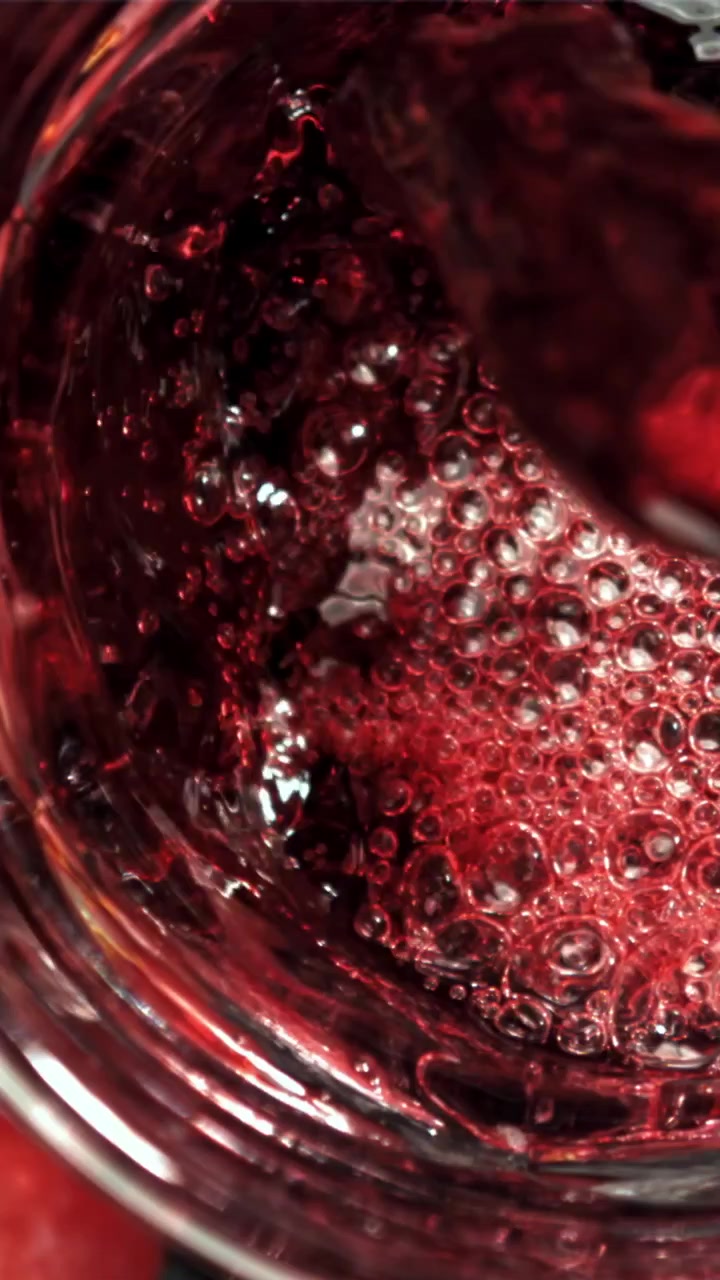 Primo piano di liquido rosso che si versa in un bicchiere con bollicine.