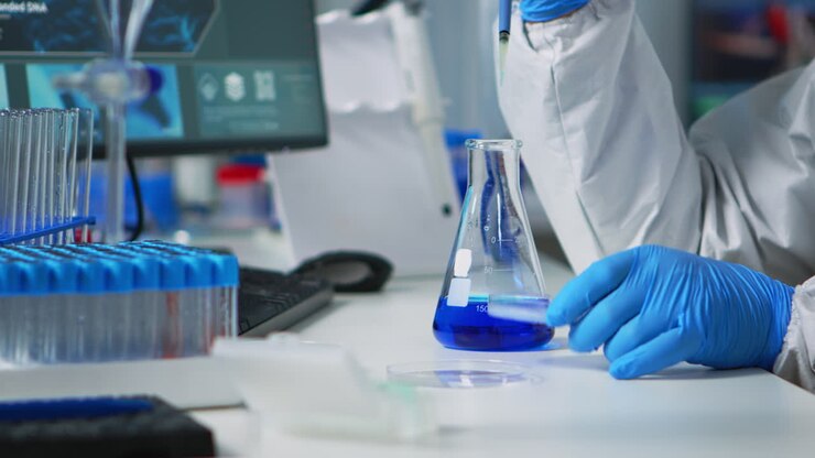 Doctor in ppe suit using pipette with microtiter plate and petri dish