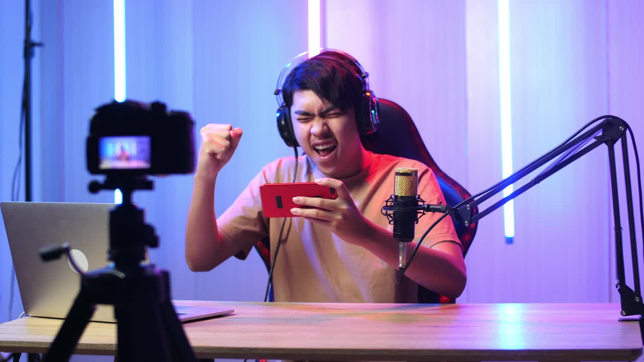 Asian Man Playing Video Game With Mobile Phone Then Celebrating While Live Stream With Camera