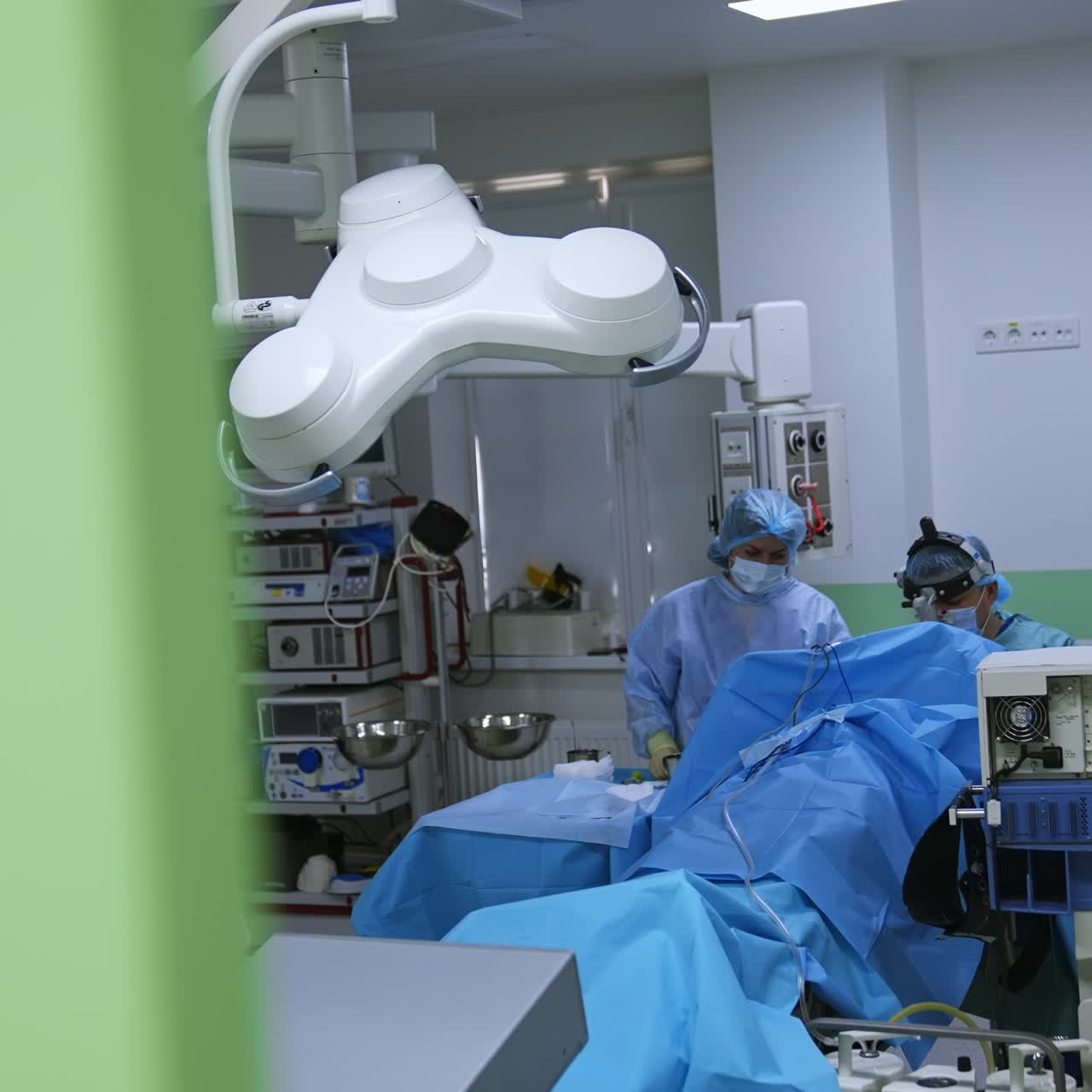 Otolaryngologist sits at the operation in surgery room. Footage at the opened doors to an operational theatre
