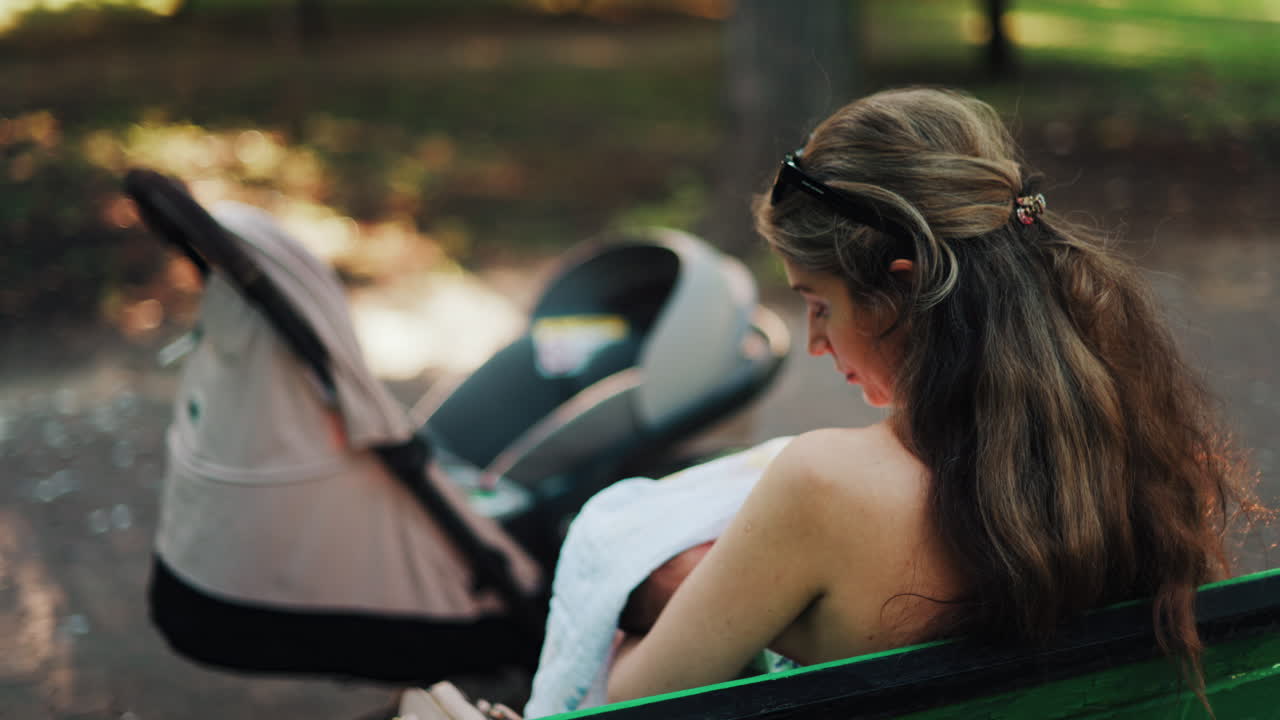 Close up of a stroller with a mother breastfeeding her baby while sitting on a park bench in the background