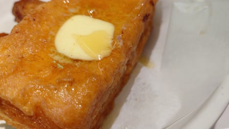 fotografía de cerca de una tostada francesa dorada con mantequilla derretida en la parte superior guardada en un plato