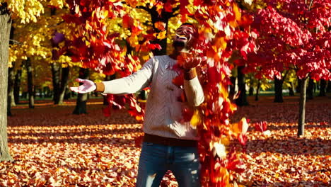 man playing in autumn leaves in a park