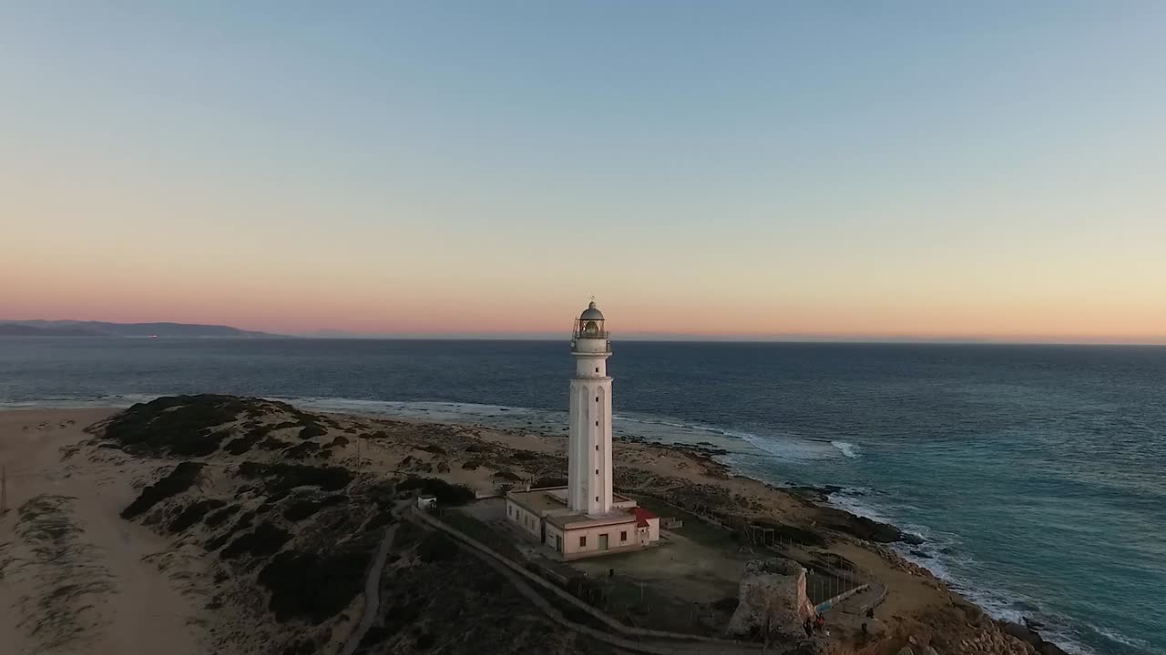 drone acercándose al faro de trafalgar post puesta de sol con el océano azul oscuro en la costa de cádiz españa