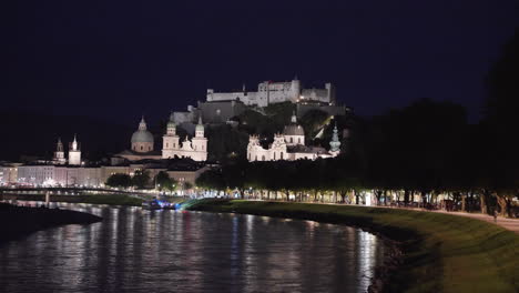 an extremely long view of fortress hohensalzburg, salzburg, austria at night when the artificial lighting is falling into the castle and a lake's water