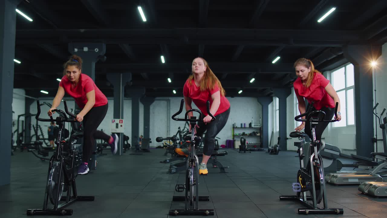 Athletic women group riding on spinning stationary bike training routine in gym weight loss indoors