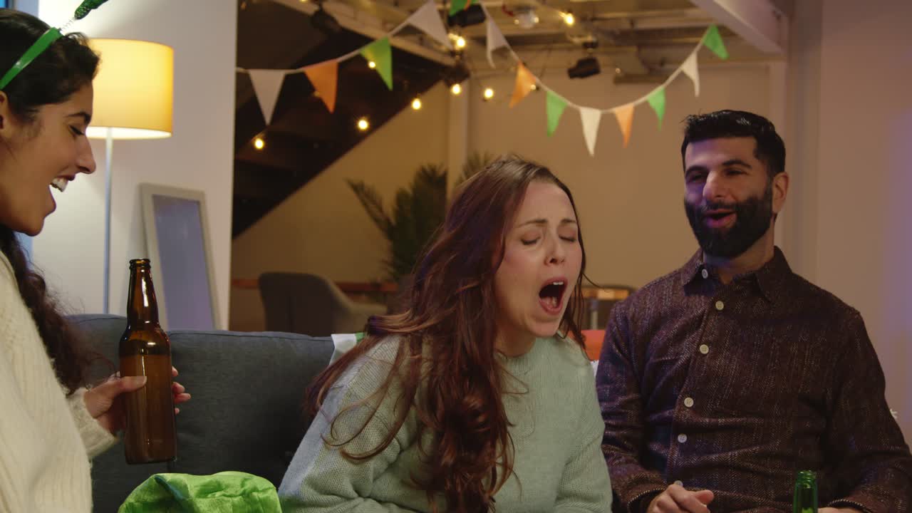 집이나 술집에서 친구 그룹이 성 패트릭의 날 파티에서 알코올을 마시고 입으로 팝콘을 잡고 축하합니다.
