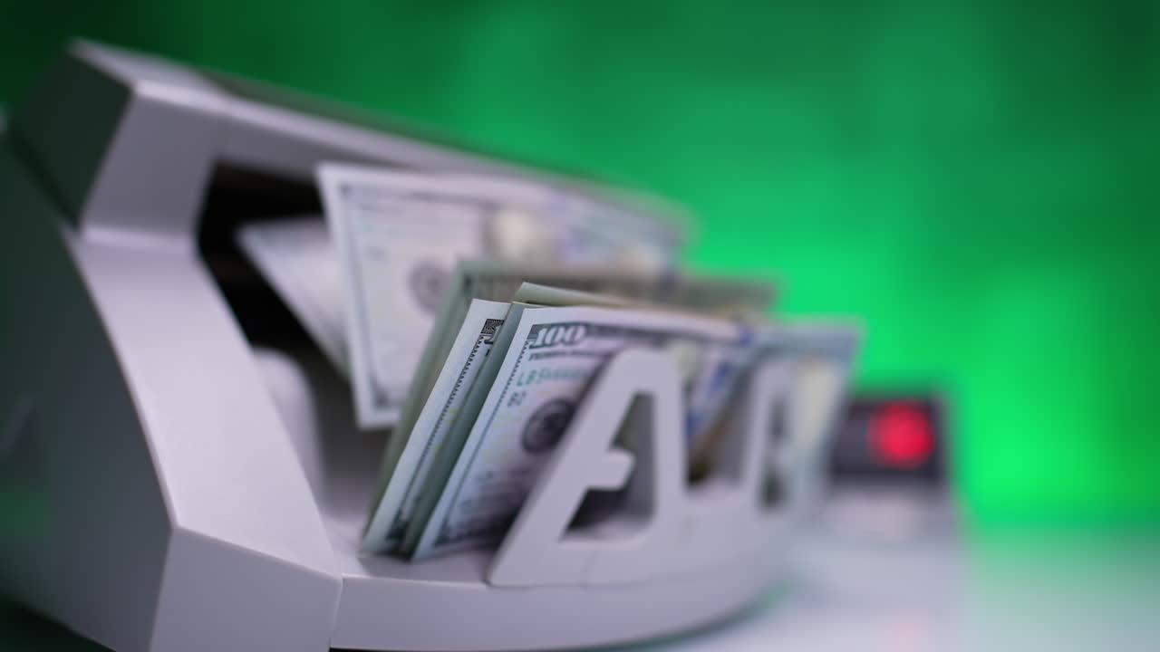 A hand touches the working cash counting machine. One hundred dollar bills appear from device. Close up. Blurred backdrop.