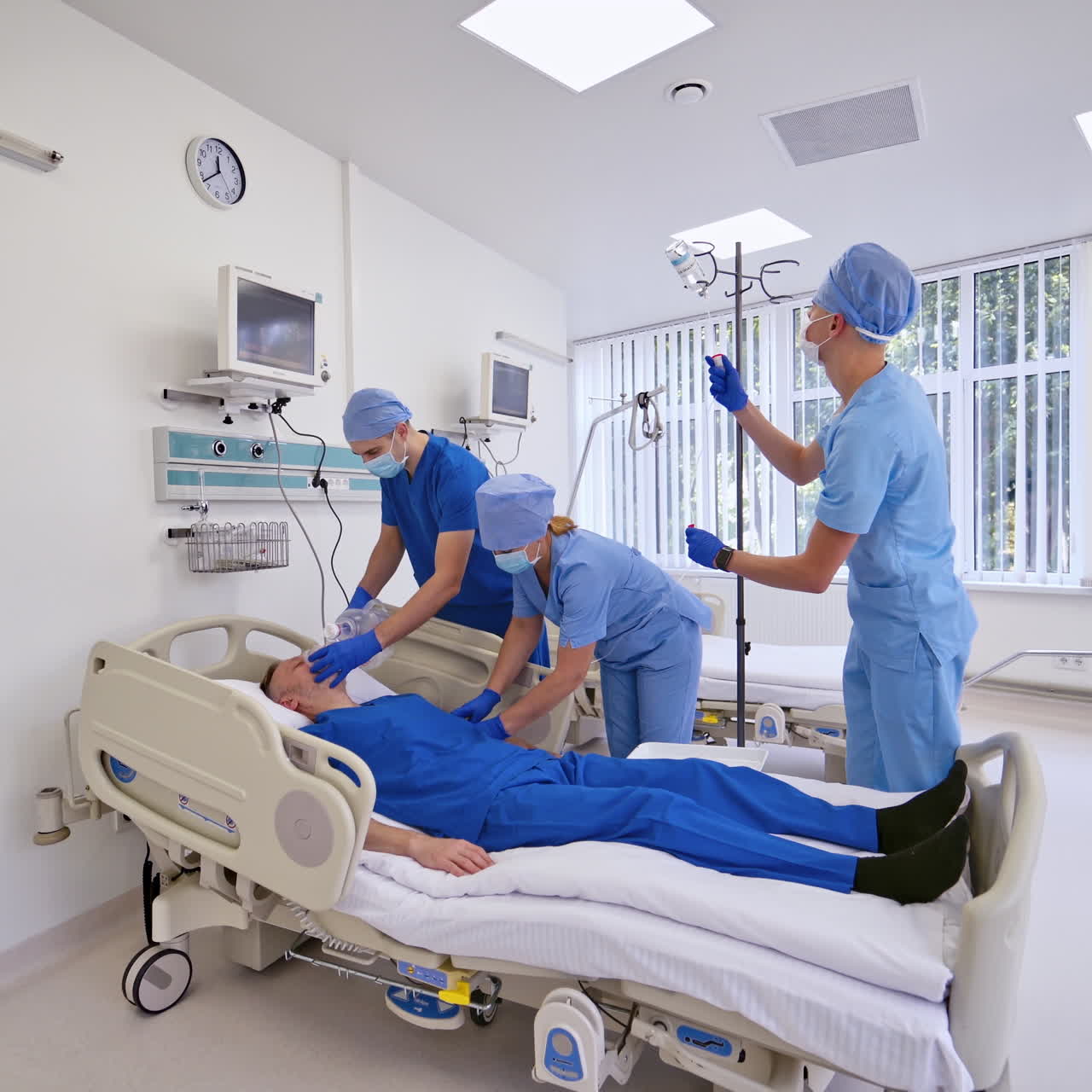 Male doctor coming into the ward with a tripod and bottle. Medical workers in special uniform giving resuscitation to a patient in the emergency room.