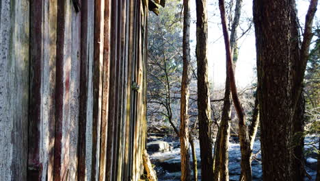 tiro inclinado hacia abajo de la fachada lateral de la cabaña de madera cerca del arroyo en el bosque