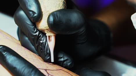 close up cámara lenta inclinación hacia abajo toma de la aguja de un artista del tatuaje penetrando la piel mientras siguen el contorno temporal de la imagen deseada en una habitación de estudio oscura