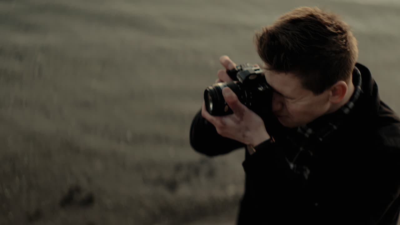 Young caucasian photographer stops to take a picture with an analog camera at a lake sunset focus