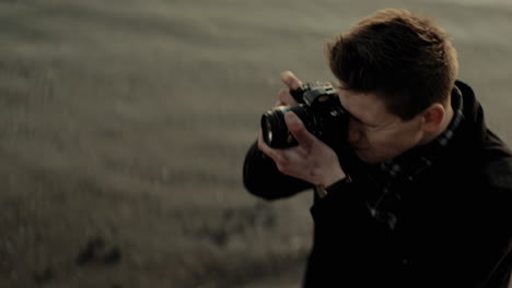 young caucasian photographer stops to take a picture with an analog camera at a lake sunset focus