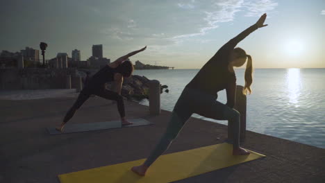 women doing yoga by the water at sunrise. slow motion.