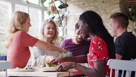 Multi-ethnic-young-adult-friends-sharing-tapas-at-lunch-together-at-a-table-in-restaurant,-low-angle