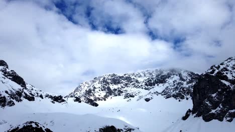 Zeitrafferkamera-Mit-Statischer-Kamera-Von-Schneebedeckten-Bergen-Mit-Blauem-Himmel-Und-Sich-Bewegenden-Wolken,-Die-überrollen-Und-Sich-Auf-Den-Berggipfeln-Verklemmen