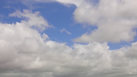 Fluffy-white-clouds-blowing-over-camera-with-patches-of-blue-sky-on-bright-windy-summer-day