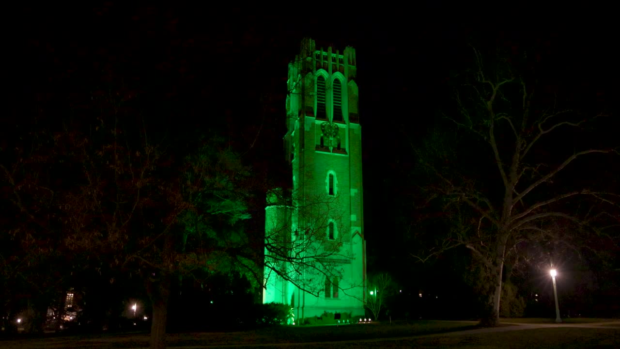 2023년 2월 비디오 안정 설정 샷으로 대량 총격 사건의 희생자를 기리기 위해 밤에 미시간 주립 대학 캠퍼스에 있는 보몬트 타워가 녹색으로 점등되었습니다.
