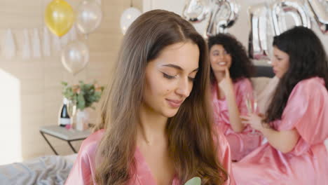 brunette woman holding bouquet, wearing pink silk nightdress, smiling and looking at camera