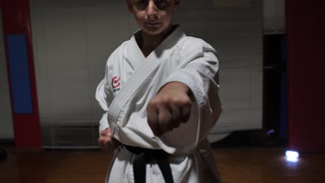 a young boy in a kimono and black belt practices his karate punch into the camera