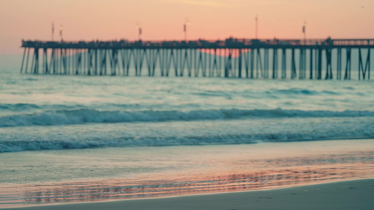 Tramonto su una spiaggia sabbiosa della California con un molo che si estende nell'oceano