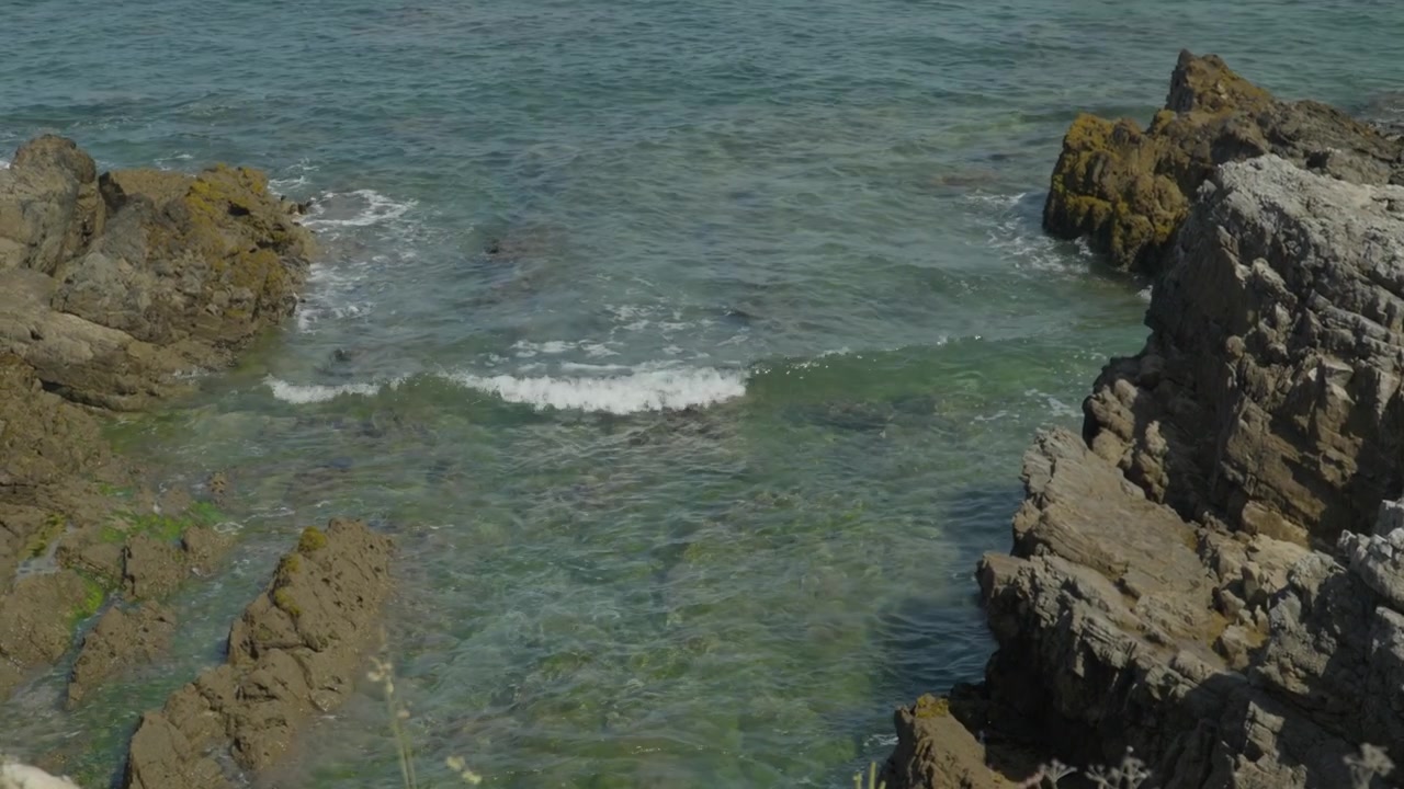 Bella ripresa dall'alto di acqua oceanica cristallina che increspa tra le aspre rocce costiere a Playa del Rinconín a Gijón, Spagna. Mette in risalto le formazioni rocciose naturali e le texture marine