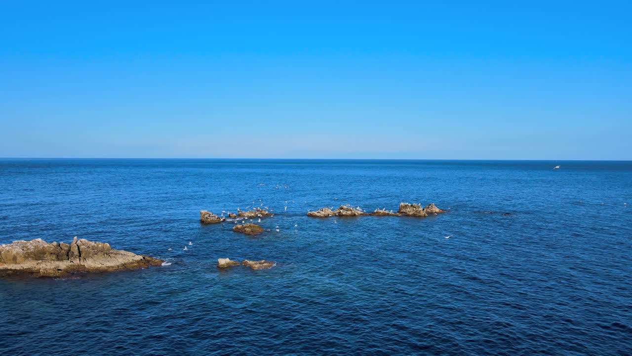 A captivating shot of a calm Moroccan coastline, featuring rugged cliffs, serene blue waters, and distant rocks under clear skies, symbolizing peace and natural beauty.