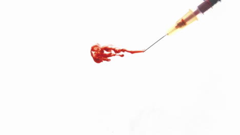 a hypodermic needle injects red liquid into clear fluid