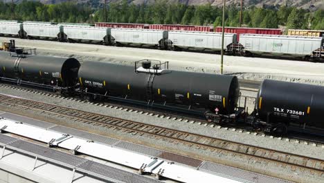 sideview dolly forward drone shot flying over railroad station in a desert environment on a sunny day over black tank trains and other cargo trailers