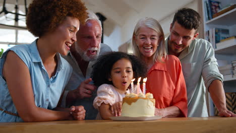 multi-generation family celebrating granddaughter's birthday at home blowing out candles on cake