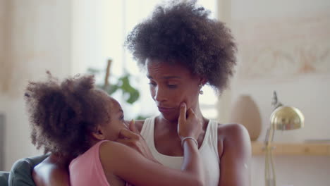 loving black woman embracing and caressing her daughter at home