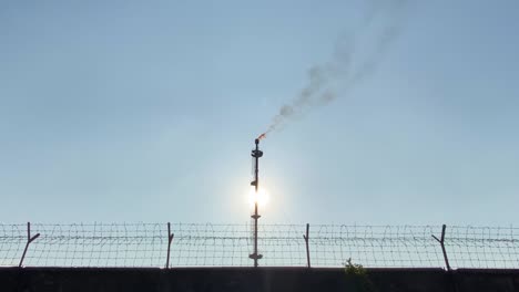 muro vallado con cable de la zona industrial, chimenea emisora de llamas de gas