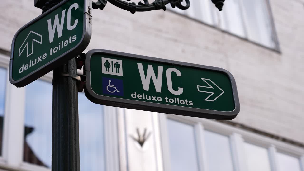 Zelená cedule na pouličním sloupu ukazuje směr k veřejným toaletám, Praha.